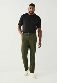 Černá košile s krátkými rukávy, olivově zelené kalhoty, černý pásek. Bílé tenisky se šedými detaily. Kalhoty mají čisté linie a kapsy.