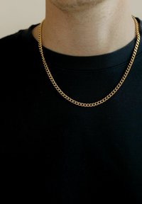 Guld kæde med sammenflettede led, der har en skinnende overflade. Båret over en sort crew-neck t-shirt. Glat tekstur med et klassisk design.
