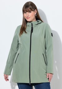 Svetlezelená bunda s kapucí, vybavená předním zipem, двумя bočními kapsami a hladkou texturou. Design zahrnuje černé akcenty a kovové doplňky.