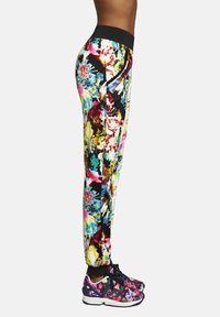 Spodnie sportowe w kwiatowy wzór z czarnym pasem, z żywymi kolorami na elastycznym materiale. W zestawieniu z pasującymi kwiatowymi sneakersami.