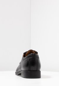 Zwarte leren schoen met een ronde neus, een gestructureerd zijpaneel en een bruine binnenkant. Voorzien van een lage rubberen zool en een subtiele logodetail.