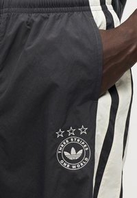 Μαύρα και λευκά σορτς Adidas με τρεις μαύρες ρίγες και κεντημένο κυκλικό λογότυπο που περιλαμβάνει τρία αστέρια και κείμενο. Ελαφρύ ύφασμα.