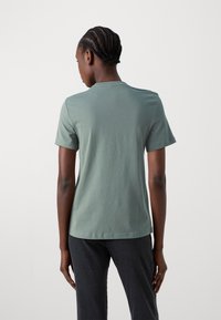 T-shirt à manches courtes en tissu de coton vert doux avec un col rond. Texture lisse, design simple sans motifs ni accents visibles.