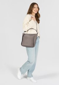 Grijze leren handtas met een gestructureerd ontwerp, voorzien van een gladde textuur en een verstelbare schouderriem, gedragen door een persoon in casual kleding.