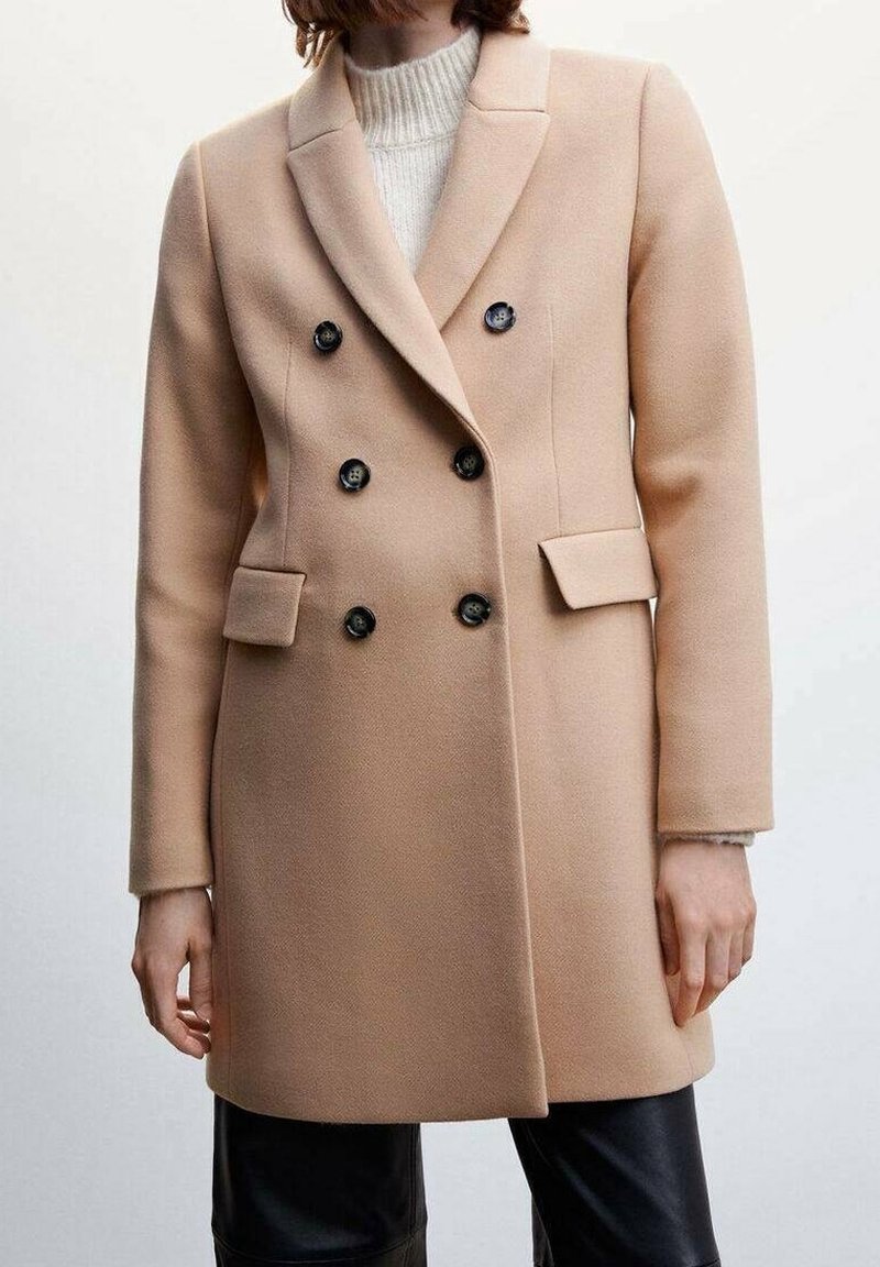Abrigo beige de doble botonadura en tejido suave, con botones negros, solapas con muesca y bolsillos frontales. Textura lisa y corte entallado.