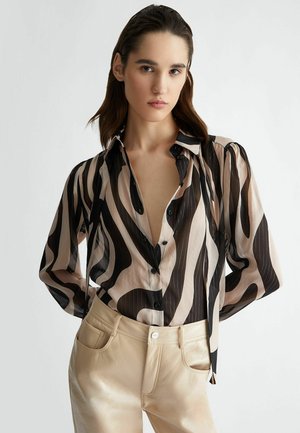 Blusa a maniche lunghe in tessuto trasparente con motivi a onde neri e crema, dotata di scollo a V profondo, patta con bottoni e maniche arricciate.
