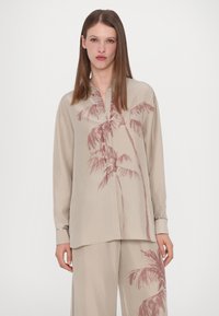 Camicia beige a manica lunga con colletto bottonato; presenta una stampa di palme in toni di rosa tenue. Tessuto morbido con una vestibilità rilassata.