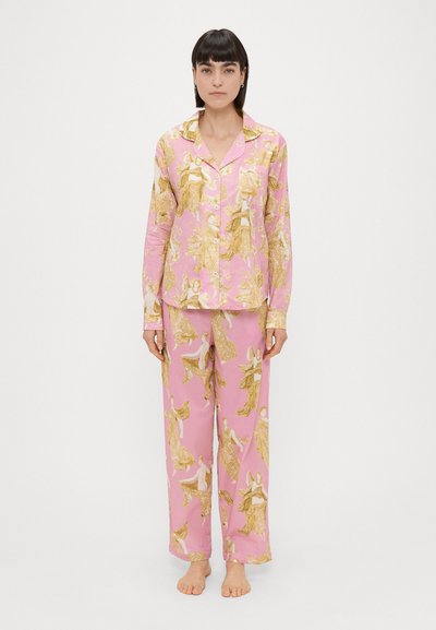 Roze pyjama-set met een knoopsluiting overhemd en losse broek, voorzien van gouden illustraties van figuren door de stof.