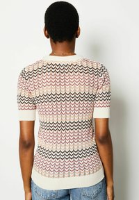 Knit top featuring a zigzag pattern in muted pink, cream, and black. Short sleeves and a ribbed neckline. Textured, lightweight fabric.