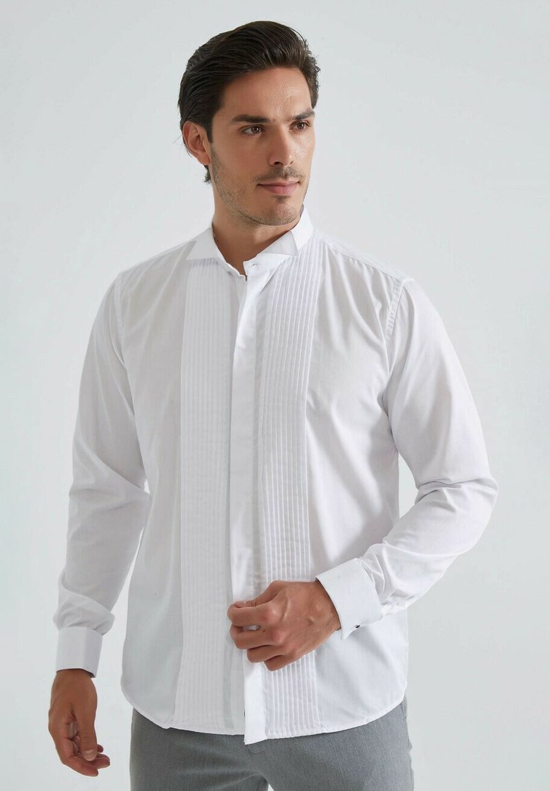 Chemise blanche à manches longues avec un devant plissé, un col classique et des poignets boutonnés. Tissu lisse avec une coupe décontractée ; sans motifs ni accents visibles.