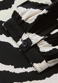 Tissu à motif noir et blanc présentant un col froncé avec une fermeture à bouton, comportant un design abstrait contrastant en texture lisse.