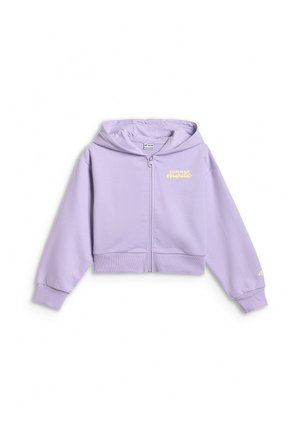 Dziecko ubrane w pastelowo fioletową kurtkę na suwak oraz szorty, żółtą koszulkę z tekstem, białe skarpetki, fioletowe sneakersy i wielokolorową czapkę, patrzy w prawo.