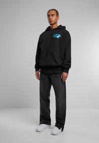 Sort hættetrøje med frontlomme, prydet med et blåt grafisk print. Kombineret med mørkegrå denim jeans og hvide sneakers. Enkel, afslappet design.