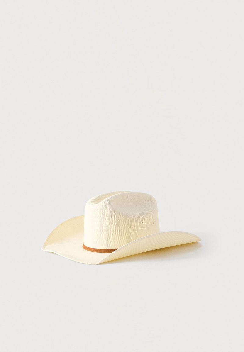 Καπέλο καουμπόι από μπεζ ψάθα με καφέ ταινία, φαρδύ κυρτό γείσο και πρησμένη κορυφή σε απλό ανοιχτό φόντο.