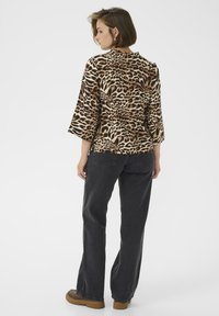 Leopardprint blouse met 3/4 mouwen, zachte stof en een scalloped halslijn, gecombineerd met hoge zwarte jeans enbruine plateau schoenen.