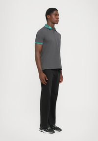 Grå polo-skjorte med en teal-mønstret krage, kombinert med svarte bukser og joggesko. Skjorten har korte ermer og en klassisk passform.