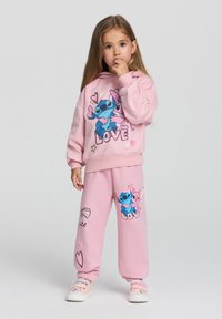 Felpa e pantaloni rosa chiaro con personaggi dei cartoni animati e testo "LOVE", polsini elastici e accenti colorati. Materiale in misto cotone.