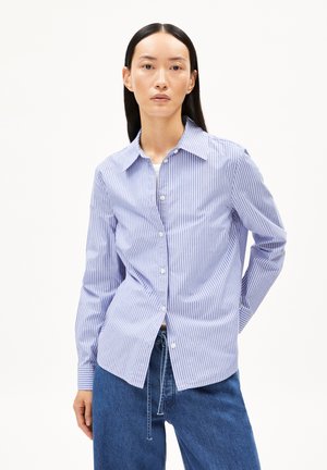 Chemise boutonnée à rayures bleues et blanches, avec un col pointu, des manches longues et une coupe ajustée. Le tissu a une texture lisse et légère.