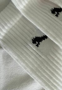 Weiße Baumwollsocken mit strukturiertem Rippmuster, versehen mit einem kleinen schwarzen Grafikdesign. Das Garn wirkt glatt und eng gewebt.
