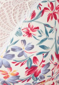 Tela con estampado floral en blanco, que presenta flores rojas, azules y amarillas. Rematada con delicado encaje blanco, mostrando intrincados detalles de diseño.