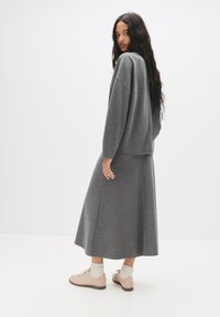 Grå to-delt sæt bestående af en løstsiddende sweater og en midi-længde nederdel. Blødt strikkemateriale med en subtil tekstur. Stylet med beige sko.