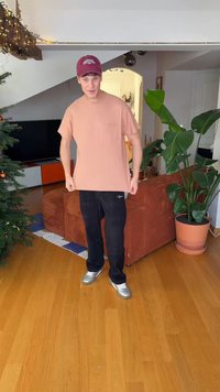 Ροζ ριμπ μπλουζάκι με τσέπη στο στήθος, συνδυασμένο με μαύρο παντελόνι και ασημένια παπούτσια, στέκεται σε οικιακό περιβάλλον κοντά σε φυτά.