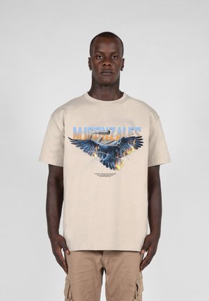 Beige bomulds T-shirt med et grafisk design af en ørn i mørkeblå med orange accenter og tekst over og under designet.