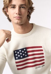 Maglione crema realizzato in tessuto a maglia con un evidente design ricamato della bandiera americana sul petto e il marchio U.S. Polo Assn.
