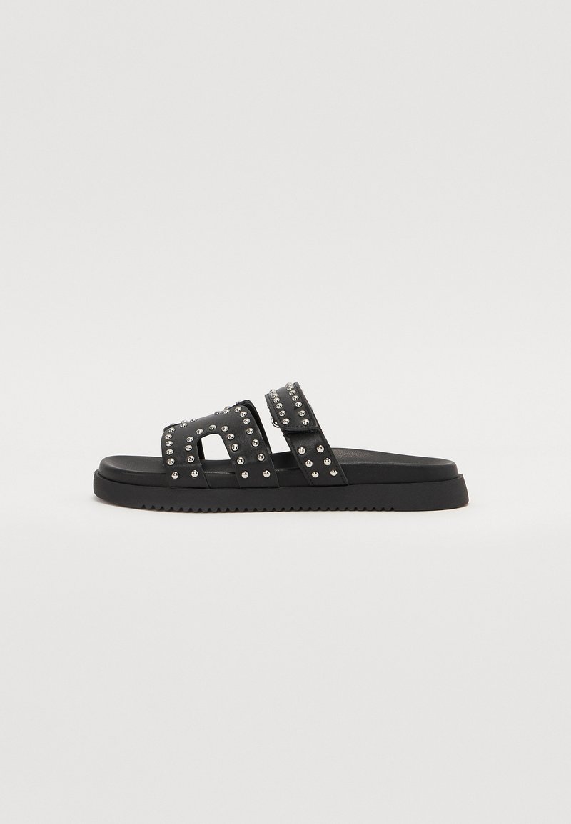 Schwarze Rutsch-Sandalen mit zwei breiten Riemen, verziert mit silbernen Nieten. Texturierten Sohle mit leichtem Profil für besseren Halt. Minimalistisches Design.