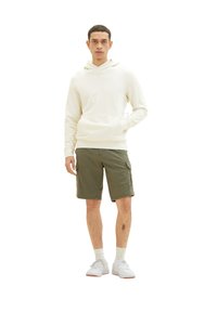 Cremefarvet hættetrøje med kængurulomme, parret med olivengrønne cargo shorts. Modellen har hvide sneakers og hvide sokker i crew-længde på. En ensfarvet baggrund.