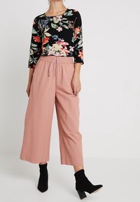 Top floreale nero con maniche a 3/4, abbinato a pantaloni a palazzo rosa chiaro. Stivali neri alla caviglia completano l'outfit.