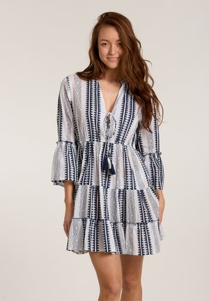 Blue and white patterned dress with a V-neck, flared sleeves, and a tiered ruffle hem. Features a tie closure with a tassel accent.