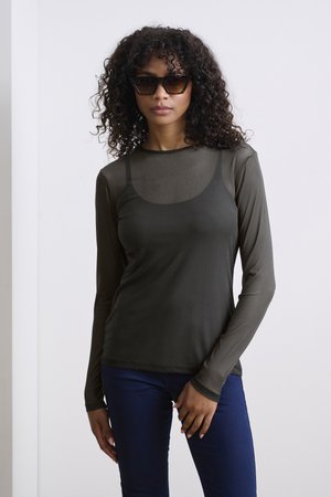 Haut à manches longues, transparent, de couleur vert olive, avec une silhouette ajustée et un col rond, associé à un jean bleu foncé. Présente une texture lisse et des détails minimalistes.