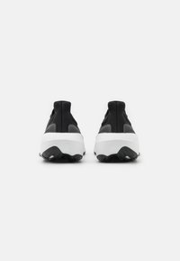 Baskets de sport noires avec une tige en tissu tricoté texturé et une semelle chunky blanche. Le talon présente une languette de traction et une marque subtile sur le côté.