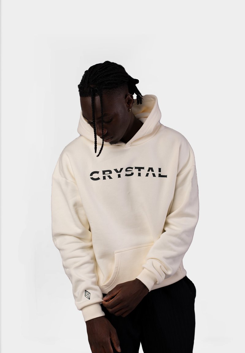 Felpa color crema con la scritta "CRYSTAL" in lettere nere, dotata di una tasca frontale e un piccolo logo a forma di cristallo sul polsino. Tessuto morbido e strutturato.