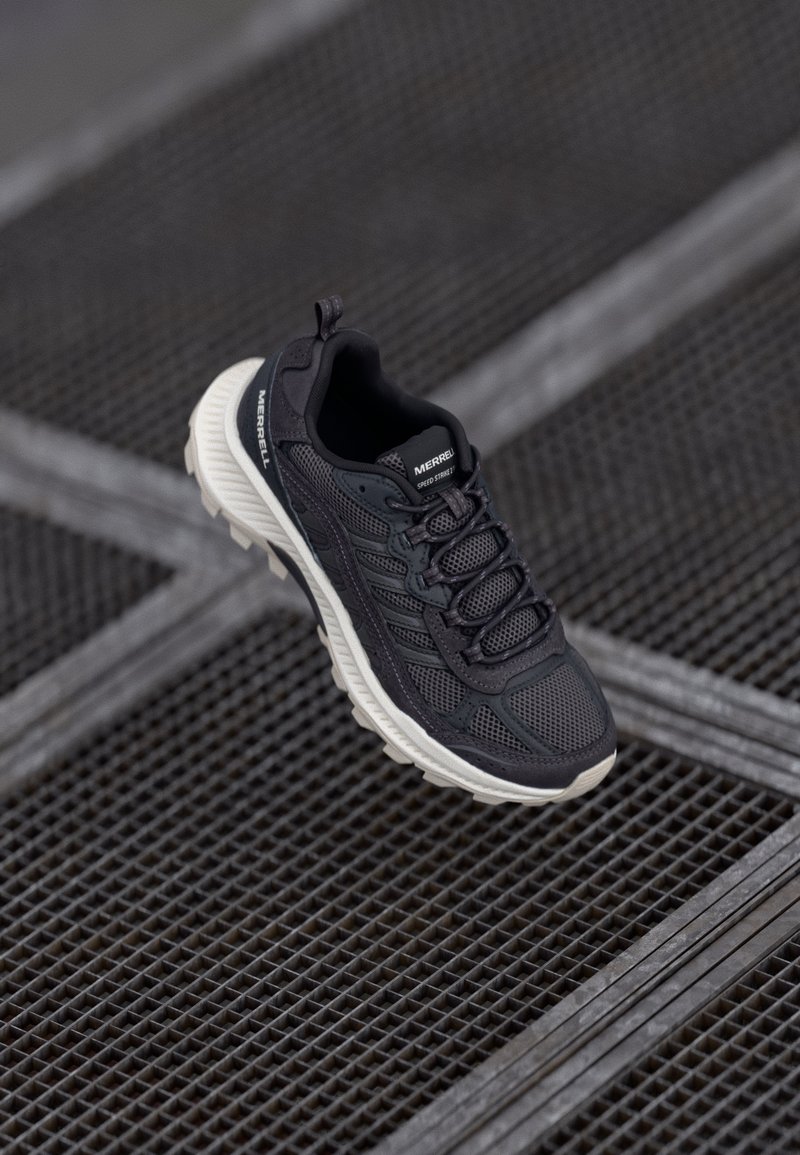 Schwarzer Mesh-Sportschuh mit strukturiertem Obermaterial, ausgestattet mit Schnürung, gepolsterter Zwischensohle und kontrastierender cremefarbener Außensohle.