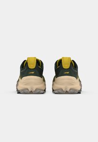 Vue arrière de chaussures de sport avec un dessus vert foncé et des accents jaunes, une semelle intermédiaire beige rembourrée et une semelle extérieure en caoutchouc avec des motifs de traction.