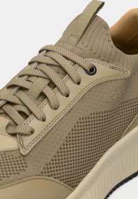 Κλείσιμο φωτογραφίας ενός ταμπά αθλητικού παπουτσιού με πλεκτό ύφασμα, υφασμάτινη πλευρική πάνελ με υφή, μπεζ κορδόνια και επενδυμένο κολάρο αστραγάλου.