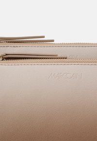 Accessoire en cuir beige avec deux fermetures éclair dorées et nom de marque Marccain embossé visible près du bord supérieur.