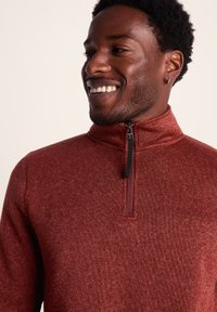 Red zip-up pullover made of textured fabric, featuring a high collar and a short zipper with a black pull tab.