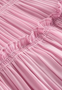 Gros plan d'un tissu rose doux avec des plis étroits et un détail de volants cousus horizontalement au centre.