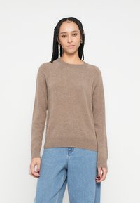 Καφέ πουλόβερ πλεκτό με μακριά μανίκια και στρογγυλή λαιμόκοψη, συνδυασμένο με ανοιχτό μπλε τζιν παντελόνι με φαρδύ πόδι· ομαλή υφή και ριγέ μανσέτες.