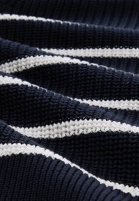 Strikket stoff med marineblå og hvite striper. Teksturert mønster med vekslende glatte og ribbete seksjoner. Myk utseende og konstruksjon.