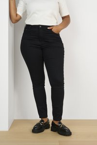 Jeans neri slim fit con vita alta, dotati di chiusura con bottone frontale e due tasche laterali. Abbinati a mocassini neri e un top bianco.