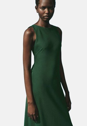 Green sleeveless dress in smooth fabric, fitted bodice, flared hem. Simple design with no visible patterns or embellishments.