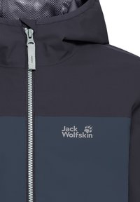 Veste imperméable bleu marine avec une fermeture éclair grise, une doublure en mesh, et le logo "Jack Wolfskin". Comprend une capuche et un design à panneaux contrastants.