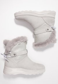 Stivali in suede grigio con un risvolto grigio peloso. Presentano un accento in pelle liscia, una suola in gomma piatta e un dettaglio in pizzo decorativo.