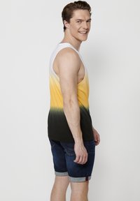 Kammita selja- ja õlavarre kaudu gradient disainiga top, mis üleminekult valgest kollase ja rohelise kuni mustani. Kandmine teksashortsidega, mille ääred on pööratud.