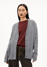Gray knitted cardigan with a v-neck and buttons down the front, worn over a maroon shirt. Features long sleeves and a relaxed fit.