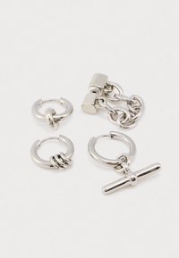 Τέσσερα ασημένια σκουλαρίκια κρίκοι με διαφορετικά σχέδια, περιλαμβανομένων δαχτυλιδιών, αλυσίδων και ενός μπιχλιμπίδι, εκτεθειμένα σε μια απλή λευκή επιφάνεια.
